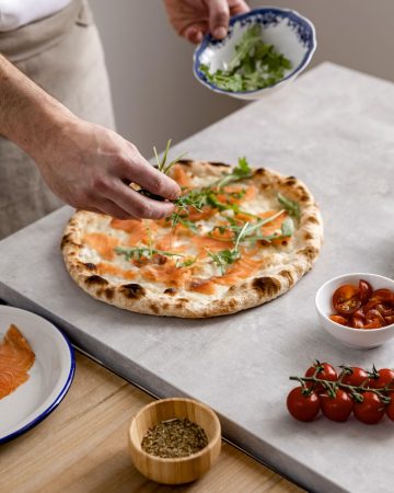 Ni Buitoni, ni Casa Tarradellas, esta es la mejor masa de pizza que vas a encontrar en Mercadona 2 Merca2.es high angle man putting arugula baked pizza dough with smoked salmon slices Merca2.es