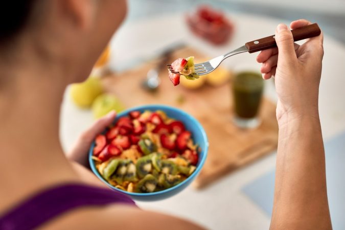 closeup athletic woman eating fresh fruit salad kitchen Merca2.es