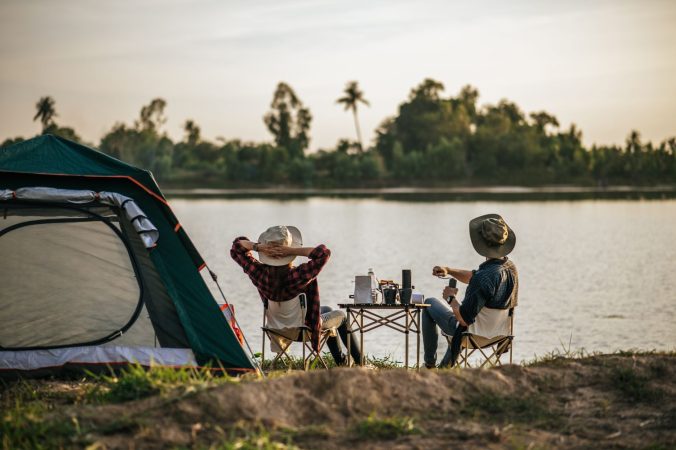 rear view young backpacker couple sitting relax front tent near lake with coffee set making fresh coffee grinder while camping trip summer vacation Merca2.es
