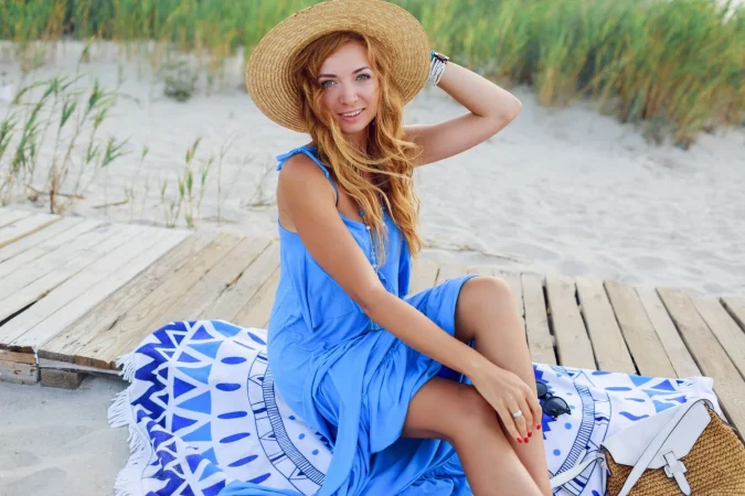 smiling redhead woman sitting beach towel perfect tan body blue dress windy hairs Merca2.es