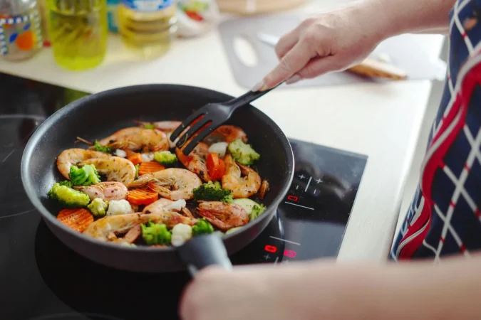 woman staying home kitchen cooking shrimps with vegetables pan home cooking healthy cooking concept Merca2.es