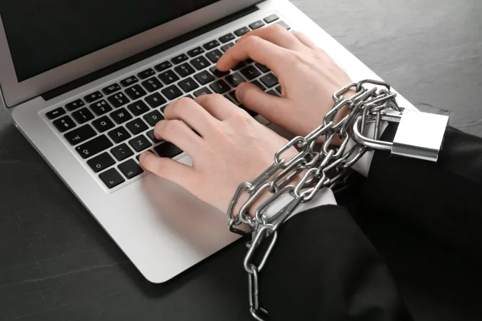 internet addiction man typing laptop with chained hands black table closeup Merca2.es