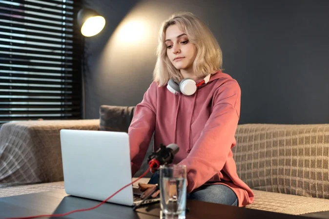 young content creator blonde girl with headphones working her laptop table with camera Merca2.es