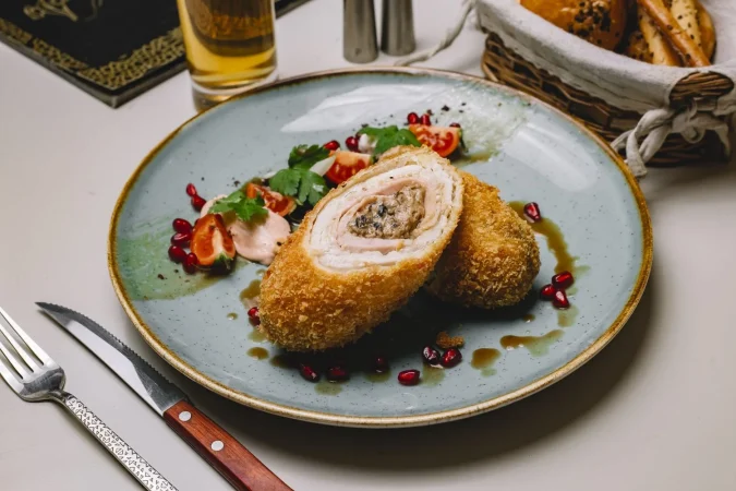 vista lateral de escalope de pollo con tomate verde granada y salsa en un plato Merca2.es