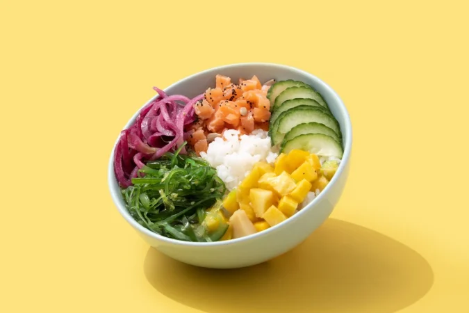poke bowl con arroz salmon pepino mango cebolla ensalada de wakame semillas de amapola y semillas de girasol aisladas sobre fondo amarillo Merca2.es