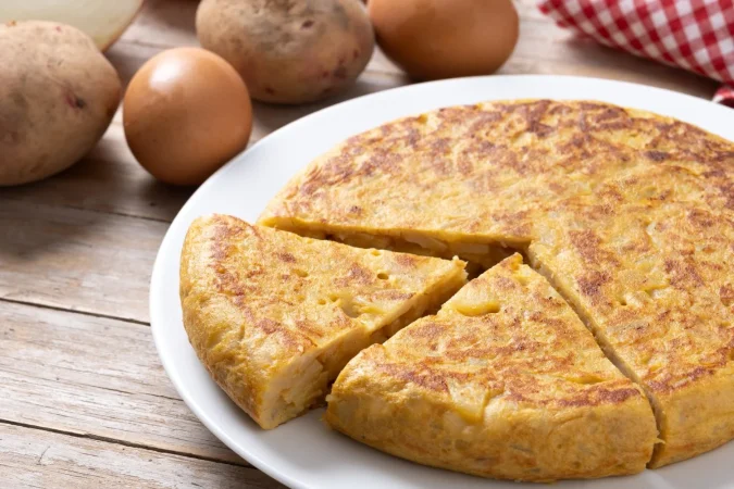 tortilla tradicional espanola con ingredientes en una mesa de madera Merca2.es