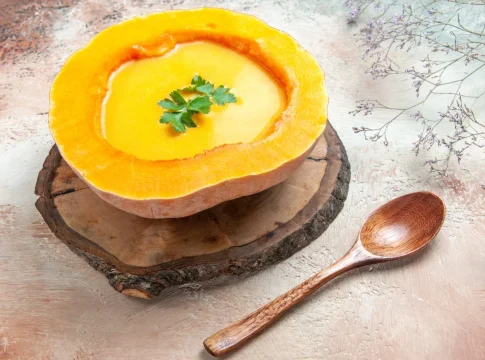 vista-lateral-de-cerca-una-sopa-sopa-de-calabaza-en-el-tablero-junto-las-ramas-de-los-arboles-de-cuchara
