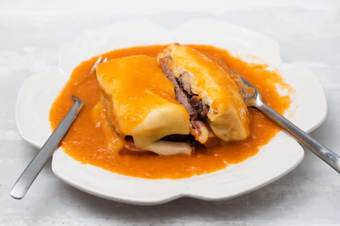 comida tipica portuguesa francesinha en plato blanco con tenedor y cuchillo Merca2.es