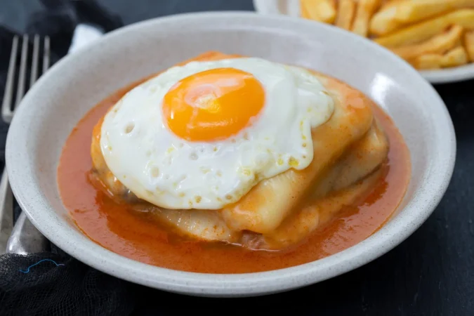 plato tipico portugues francesinha en plato sobre fondo de ceramica negra Merca2.es