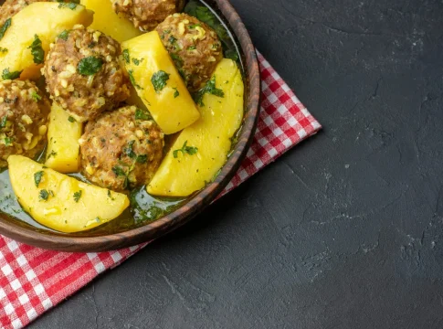 vista-superior-de-una-cena-sabrosa-con-albondigas-papas-verdes-en-un-tazon-marron-sobre-una-toalla-roja-pelada-sobre-fondo-negro-con-espacio-libre