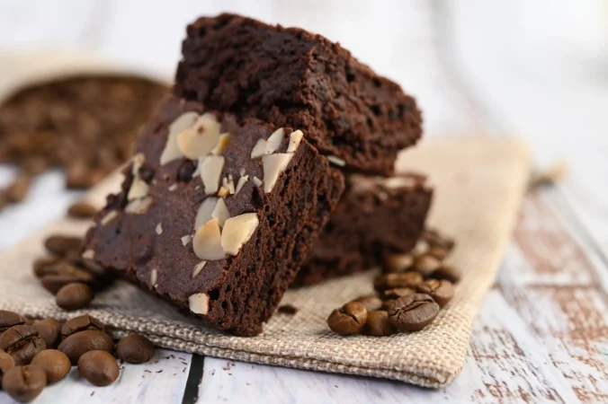brownie de chocolate en cilicio y granos de cafe sobre una mesa de madera Merca2.es