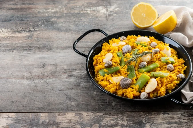 paella valenciana tradicional con pollo de conejo garrofon frijoles caracoles frijoles verdes marroquies y azafran en mesa de madera Merca2.es