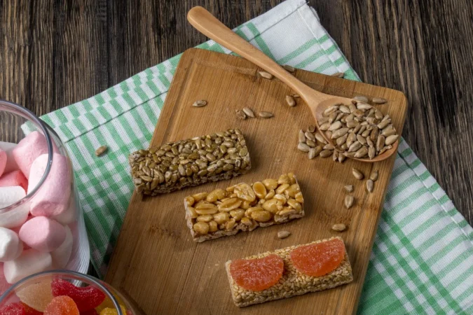 Barritas energéticas caseras: la receta fácil que te dará energía todo el día 3 Merca2.es vista lateral de dulce kozinaki de semillas de girasol sesamo y mani sobre una tabla de madera y con malvaviscos de colores en un frasco de vidrio en rustico Merca2.es