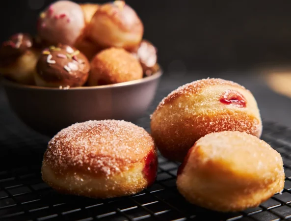 Cómo preparar berlinas de fresa caseras, el capricho más tierno y delicioso 1 Merca2.es donuts fritos con azucar y crema sobre una mesa negra 1 Merca2.es