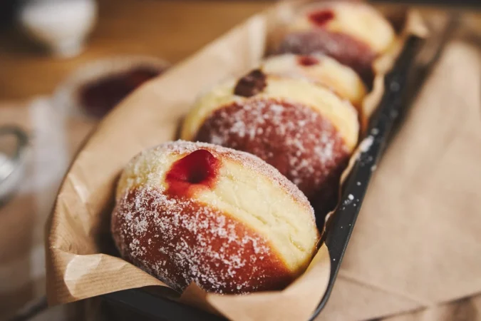 Cómo preparar berlinas de fresa caseras, el capricho más tierno y delicioso 2 Merca2.es primer plano de donuts esponjosos con mermelada en un recipiente bajo las luces Merca2.es