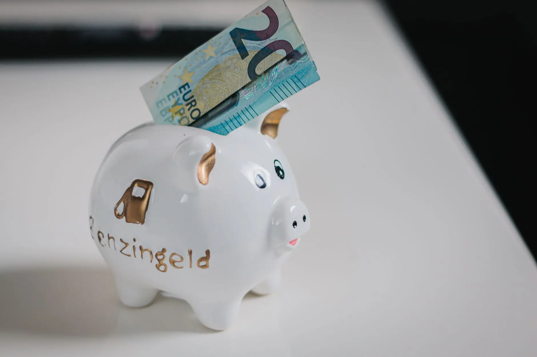 Una hucha blanca con un billete de €20 insertado, simbolizando ahorros.