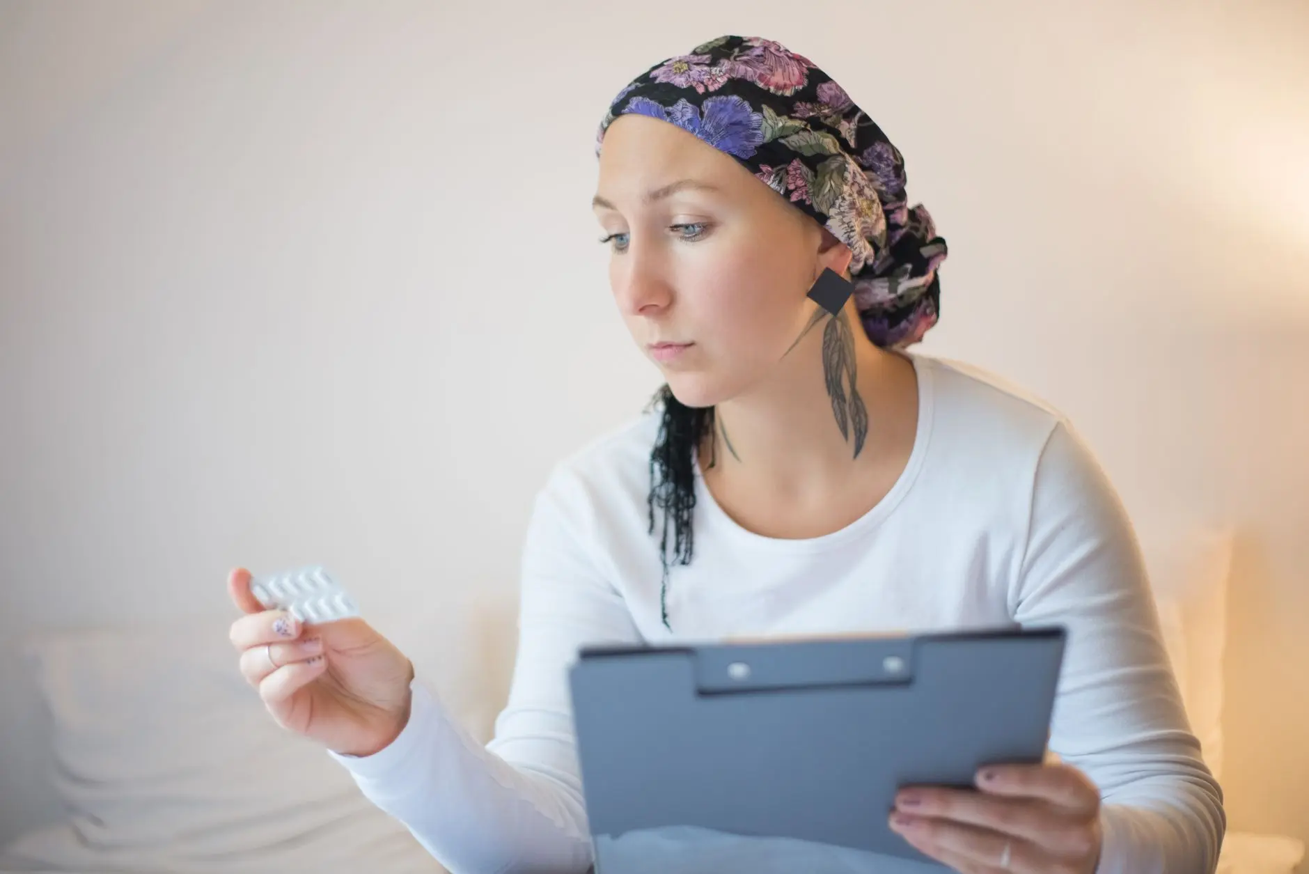 Mujer con pañuelo en la cabeza revisa medicamentos en el dormitorio, simbolizando esperanza y recuperación.