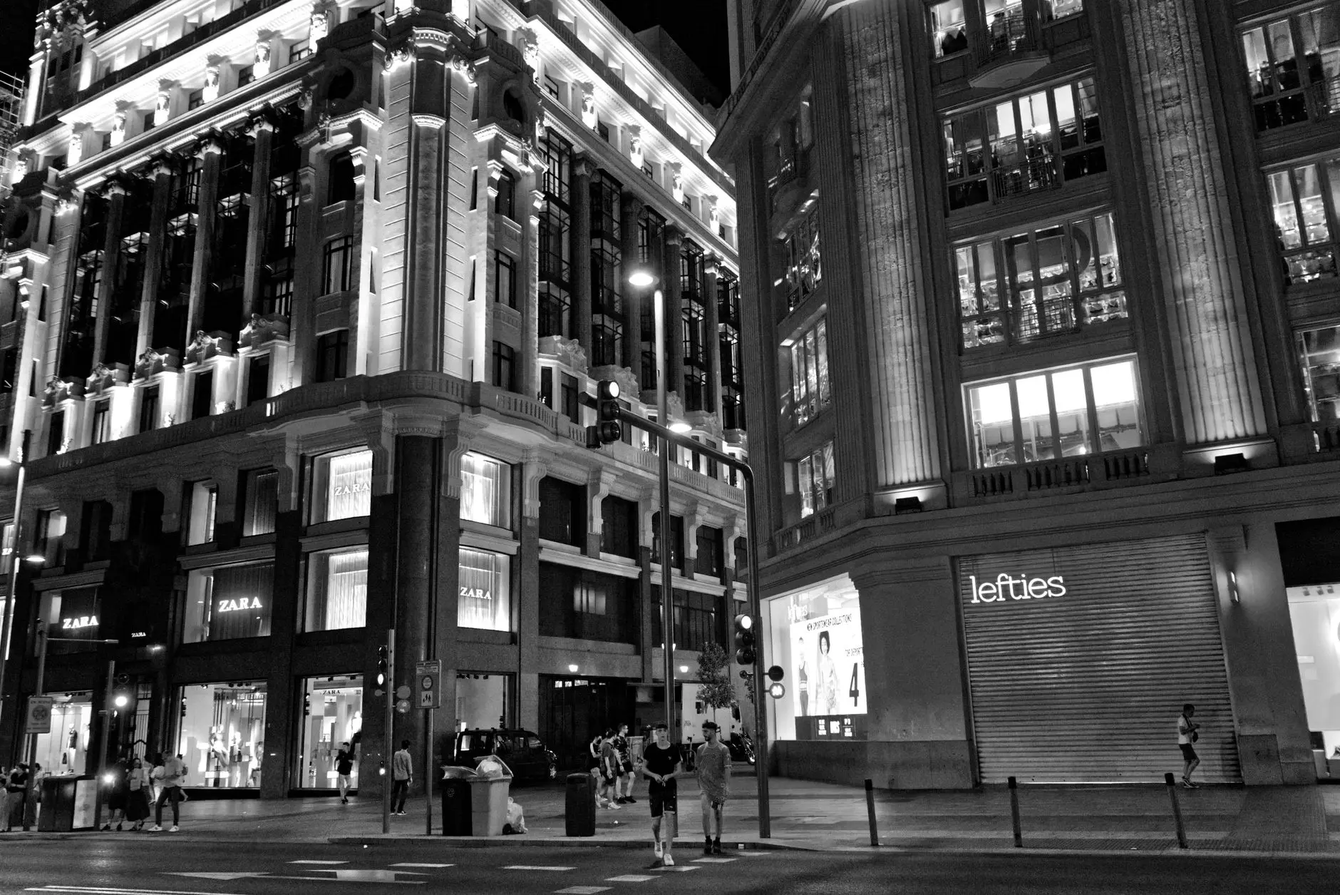 Vista nocturna en blanco y negro de la Gran Via, Madrid, mostrando la arquitectura histórica iluminada.