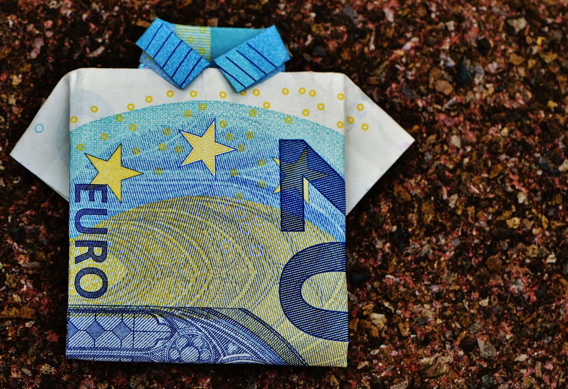 Un billete de 10 euros doblado en una camiseta de origami sobre un fondo texturizado que muestra creatividad.