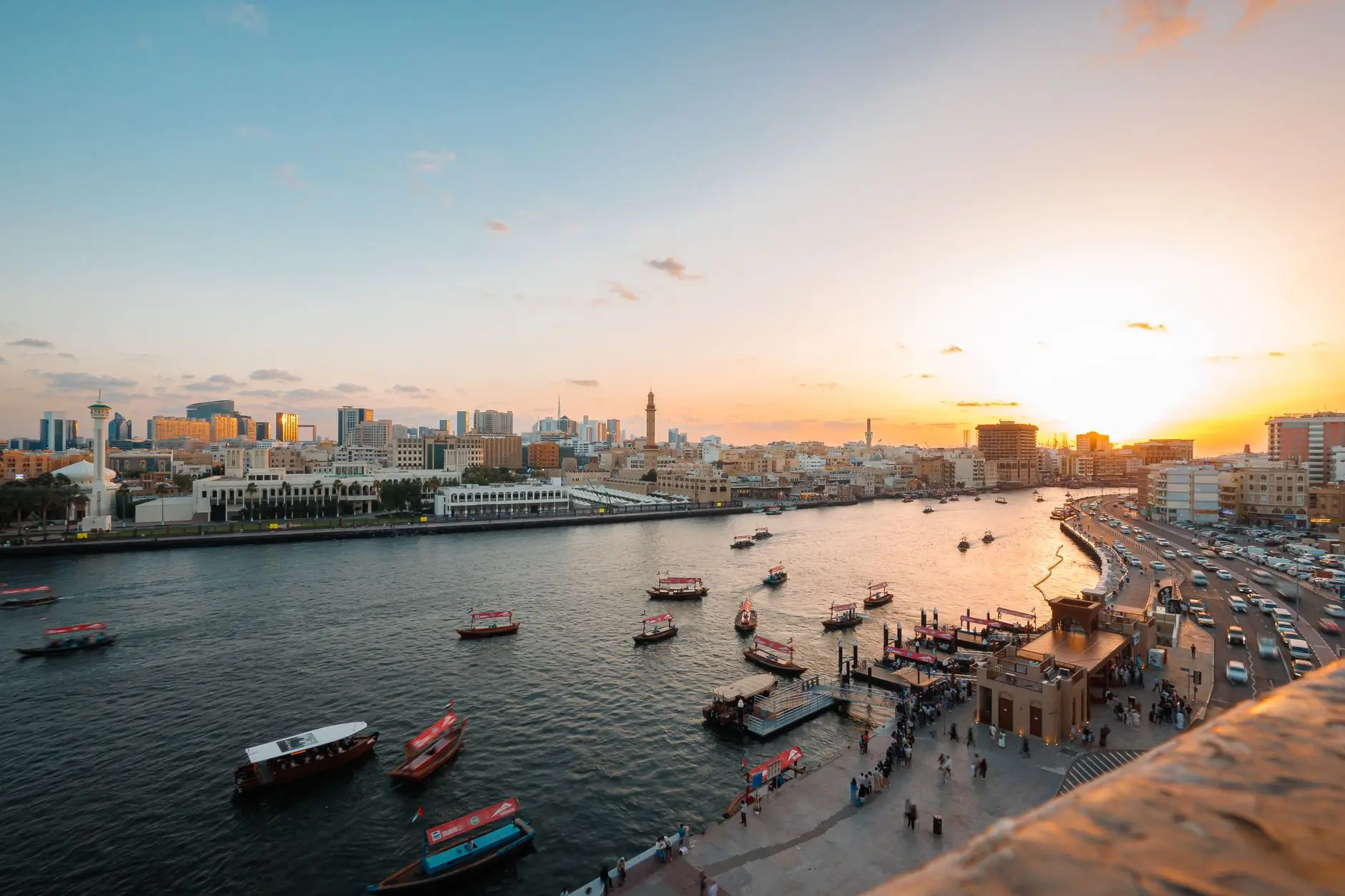 Impresionante puesta de sol sobre Dubai Creek con barcos tradicionales y un paisaje urbano vibrante.