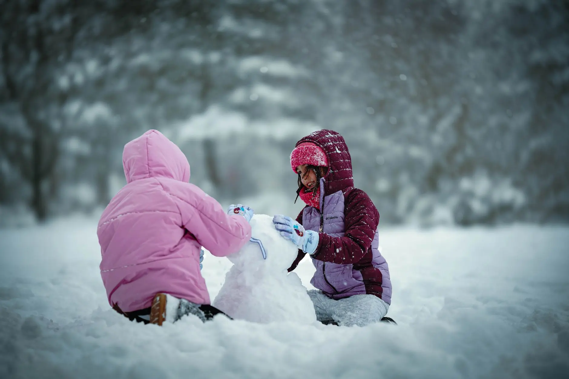 Dos niños disfrutan del invierno construyendo un muñeco de nieve en un parque nevado.