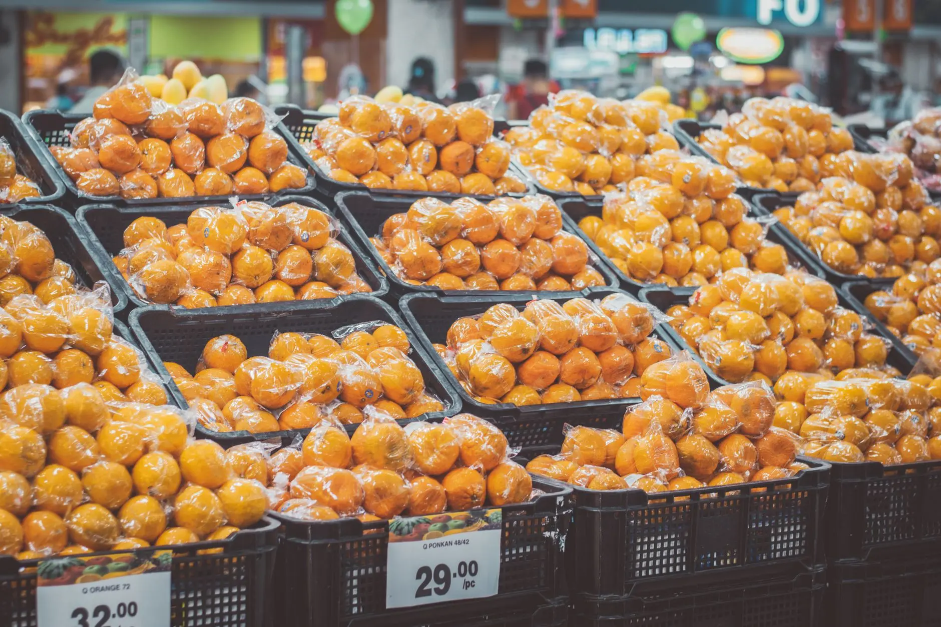 Montículo de naranjas frescas envueltas en plástico en una tienda, con precio etiquetado.