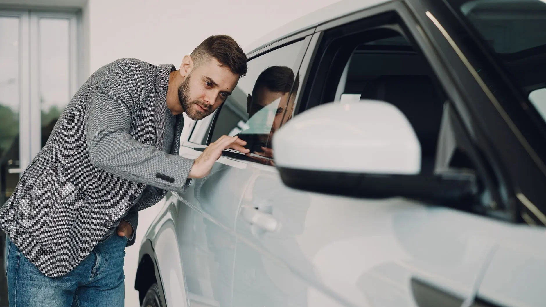 Hombre examinando detenidamente un coche blanco moderno en el showroom del concesionario.