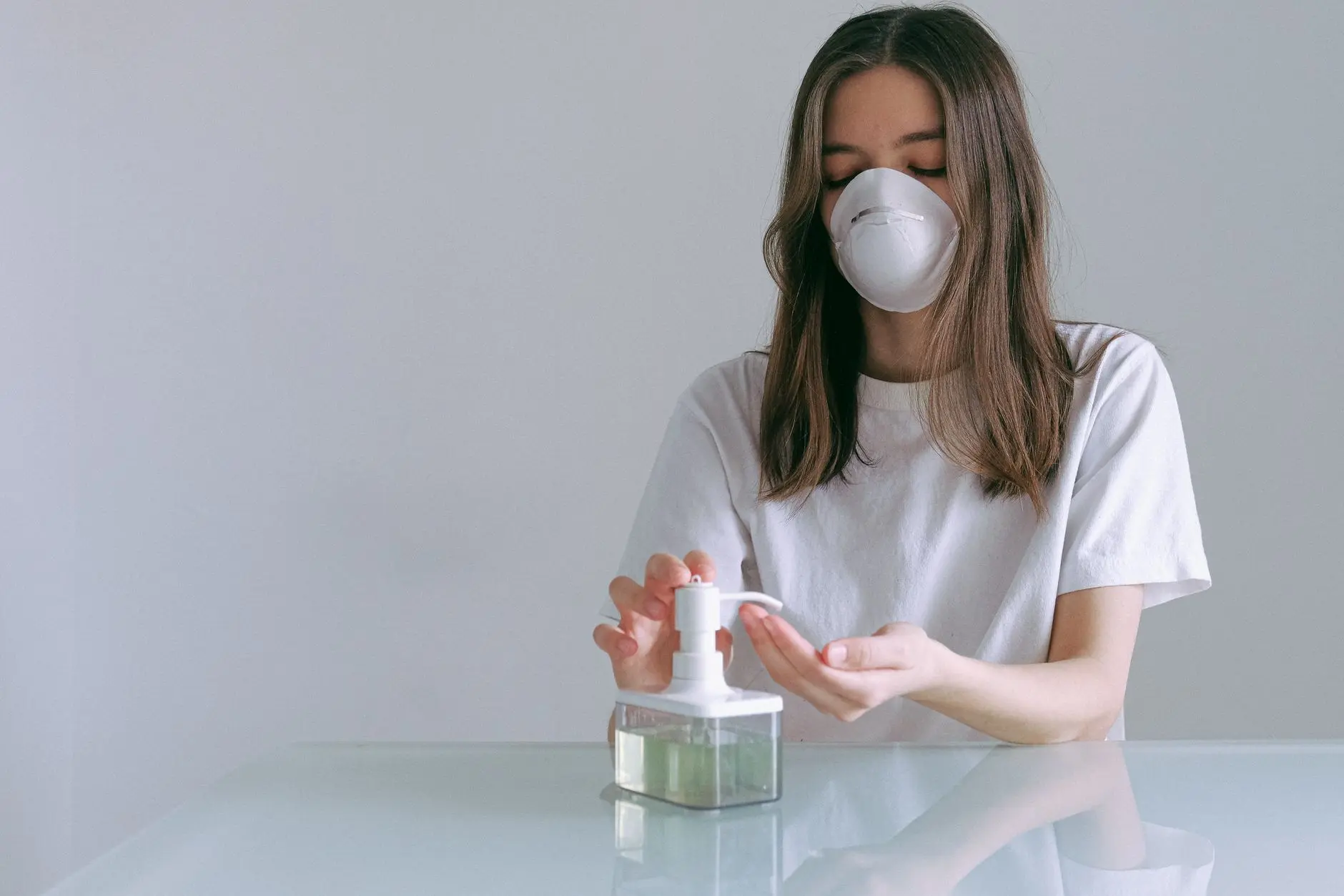 Mujer practicando la higiene con gel hidroalcohólico y mascarilla en casa durante la pandemia.