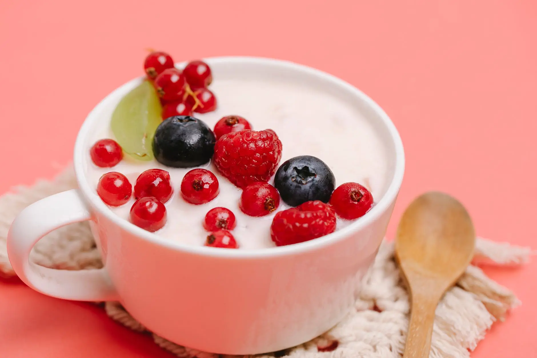 Un delicioso tazón de yogur cubierto con frutas del bosque frescas sobre una superficie rosa.