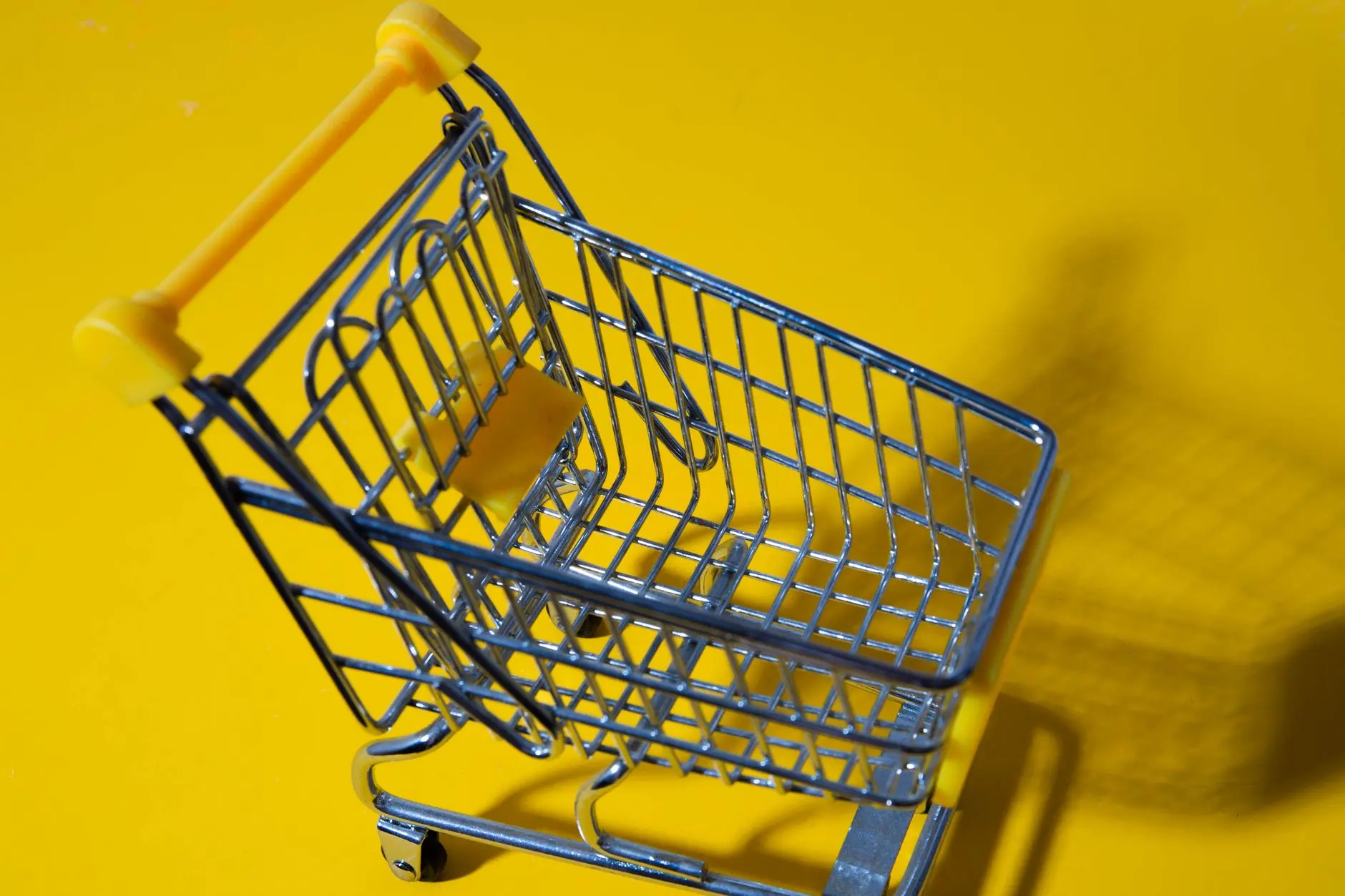 Primer plano de un pequeño carrito de compras de juguete sobre un fondo amarillo vibrante.