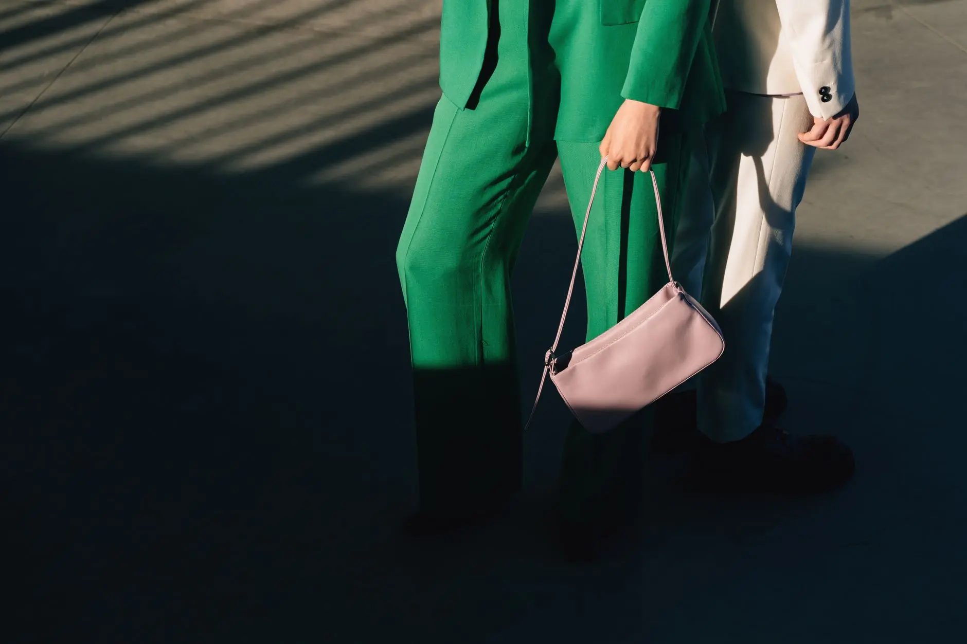 Pareja de moda en trajes verde y blanco con bolso rosa en un entorno sombrío.