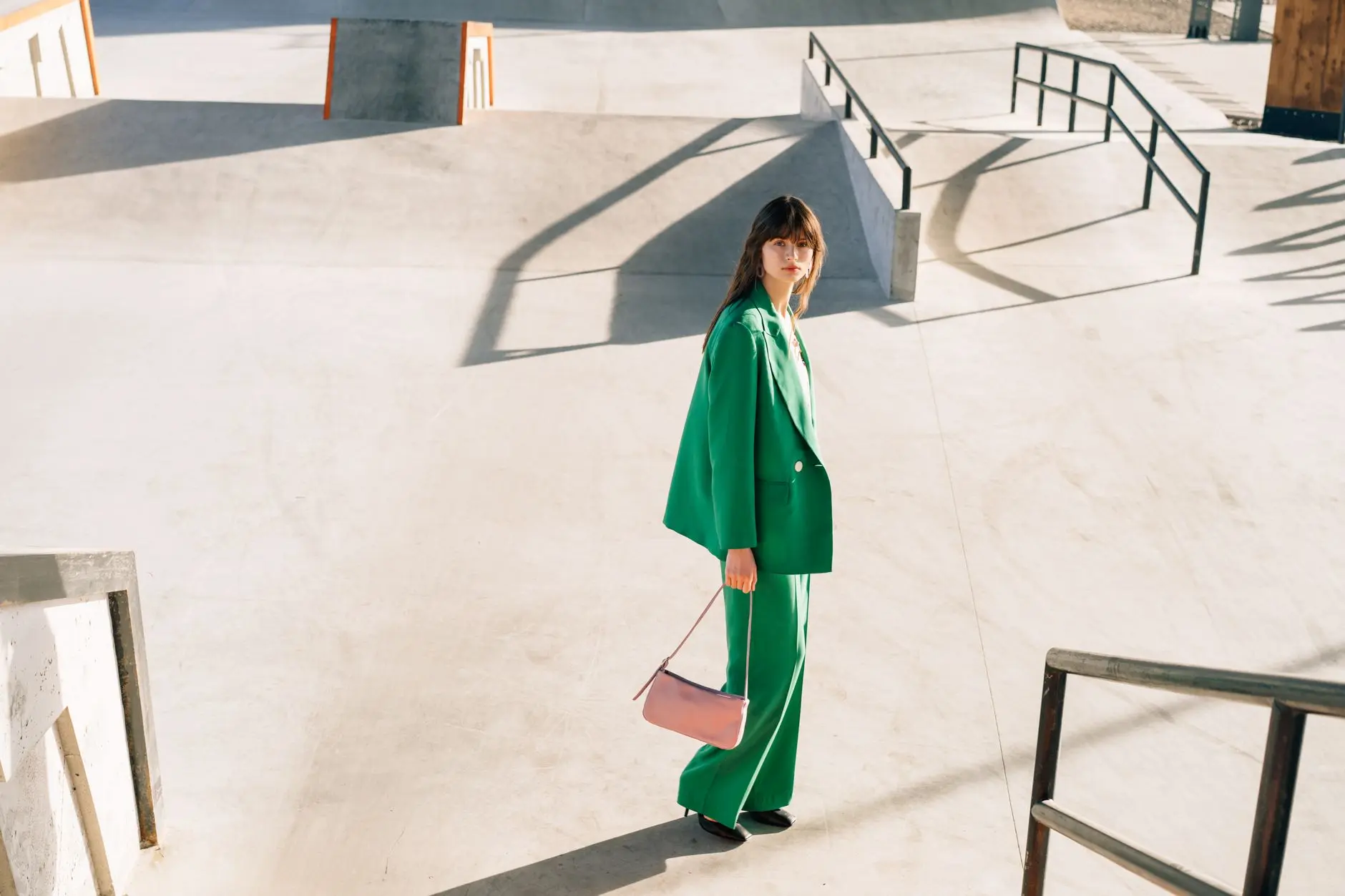 Mujer de moda en traje verde con bolso rosa posa en ubicación urbana al aire libre, mostrando un estilo moderno.