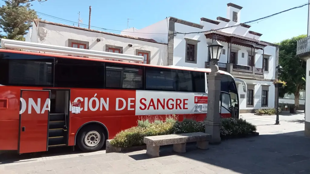 Autobús rojo de donación de sangre estacionado frente a un edificio blanco