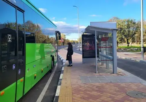 Autobús verde junto a una marquesina Una persona junto a una marquesina y un autobús verde en la parada.