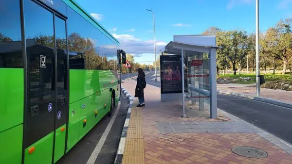Autobús verde junto a una marquesina Una persona junto a una marquesina y un autobús verde en la parada.
