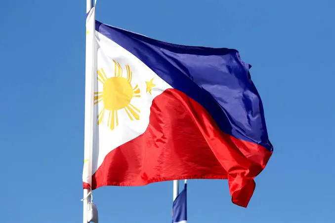 Bandera filipina ondeando bajo el cielo azul Bandera de Filipinas ondeando en un mástil frente a un cielo azul.