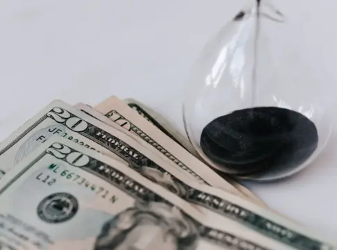 Dólares junto a un reloj de arena Primer plano de billetes de dólar y reloj de arena simbolizando el concepto de tiempo y dinero.