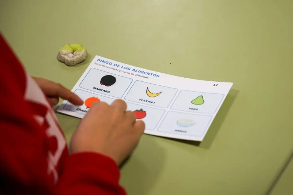 Una mano marca una casilla en un cartón de bingo ilustrado con alimentos.