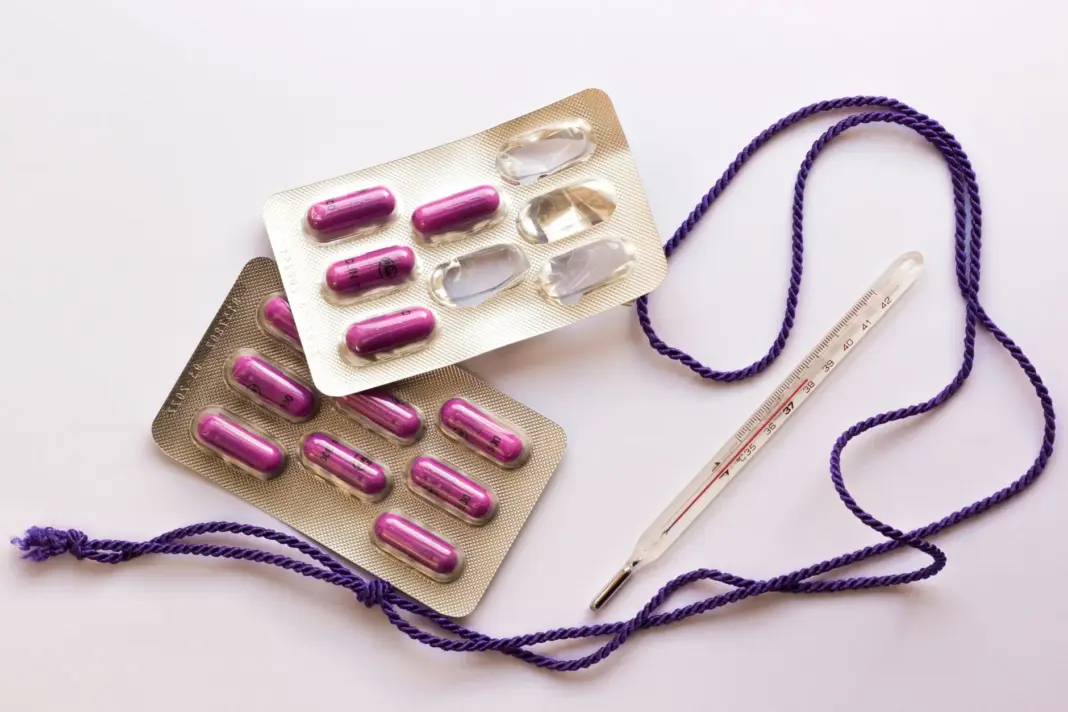 Imagen de píldoras y un termómetro sobre un fondo blanco, útil para temas de salud.