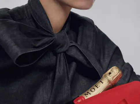 Botella Moët con lazo rojo Persona sostiene una botella Moët junto a un gran lazo rojo de regalo.
