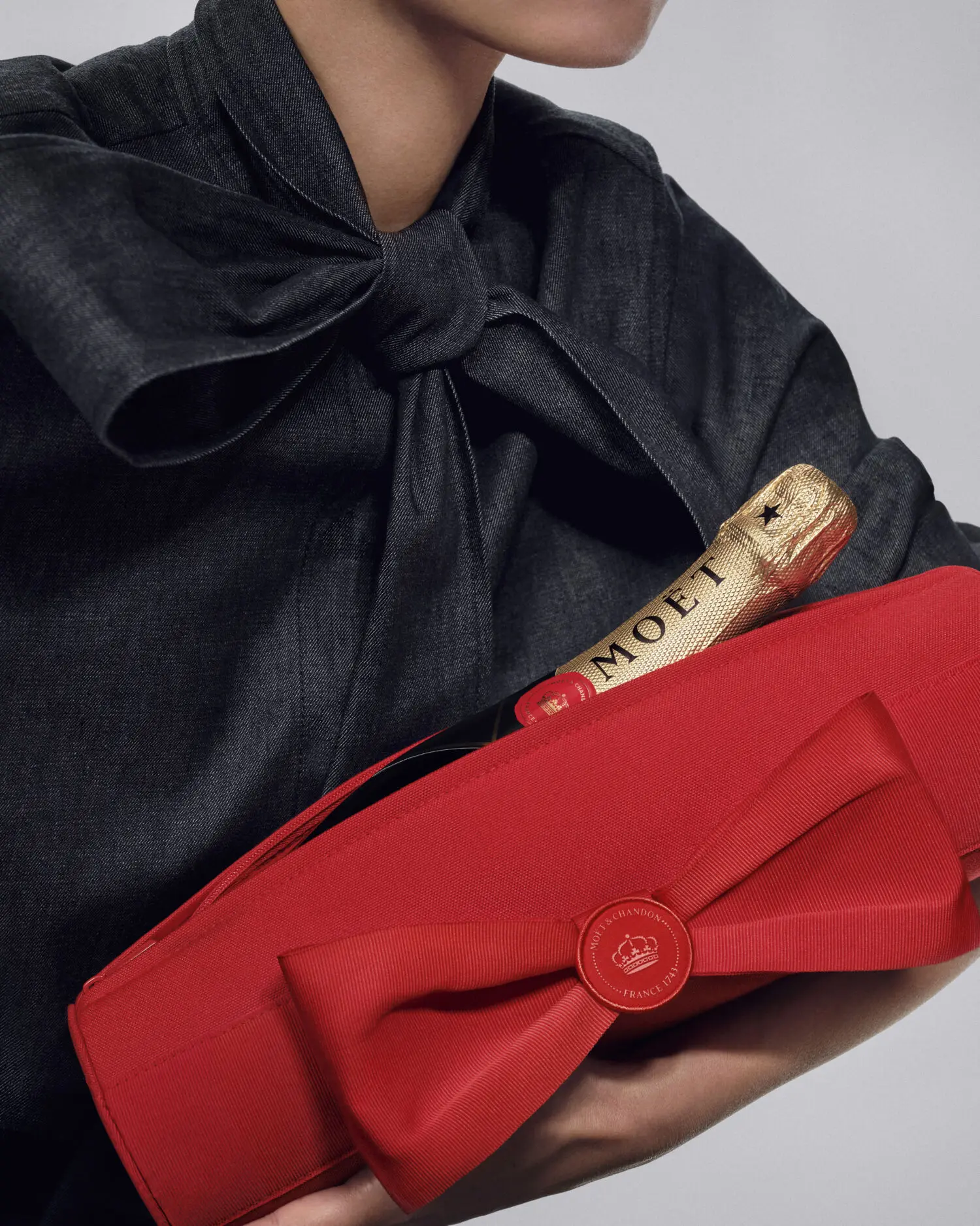 Persona sostiene una botella Moët junto a un gran lazo rojo de regalo.
