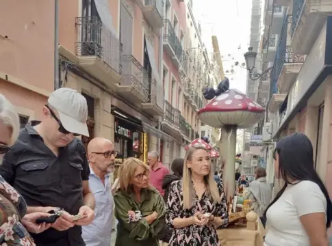 Puesto callejero en Botigues al Carrer Varias personas miran accesorios y artículos variados en un puesto callejero bajo adornos de setas.