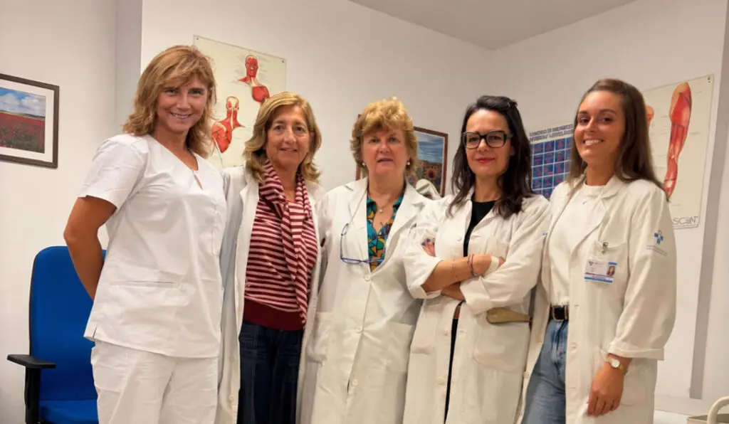 Cinco mujeres posan en una sala con batas blancas y carteles anatómicos.