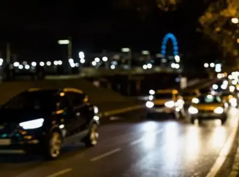 Coches circulando de noche con los faros encendidos Varios coches circulan de noche por una vía urbana con los faros encendidos.