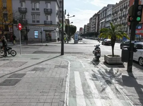 Cruce urbano con ciclista y tráfico Cruce urbano con una persona en bicicleta, un scooter, coches y semáforos.