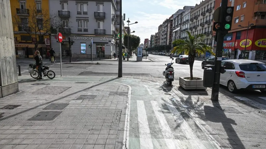 Cruce urbano con ciclista y tráfico Cruce urbano con una persona en bicicleta, un scooter, coches y semáforos.