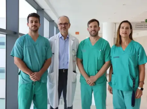 Cuatro personas en un pasillo hospitalario Cuatro personas posan en un pasillo hospitalario; tres llevan uniformes clínicos y una bata blanca.