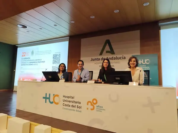 Mesa de ponencias en el Hospital Costa del Sol Cuatro personas sentadas en una mesa de ponencias en un auditorio hospitalario.