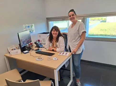 Dos mujeres en una habitación Dos mujeres posan junto a un escritorio con ordenador y varios objetos.