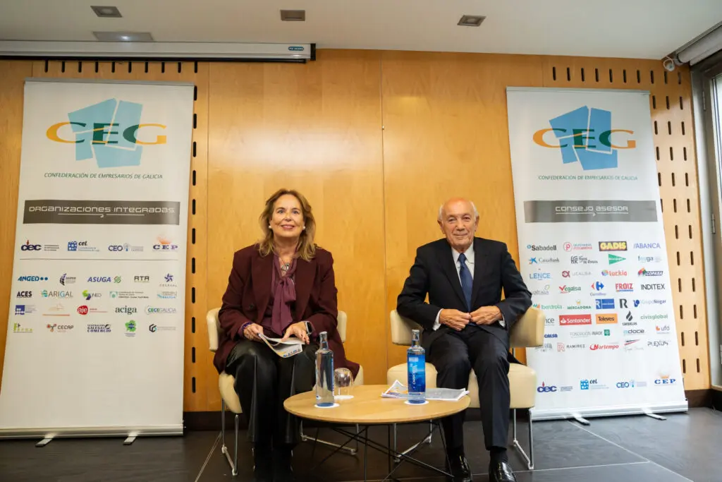 Dos personas entre paneles de la CEG Dos personas sentadas junto a una mesa, entre paneles de la CEG.